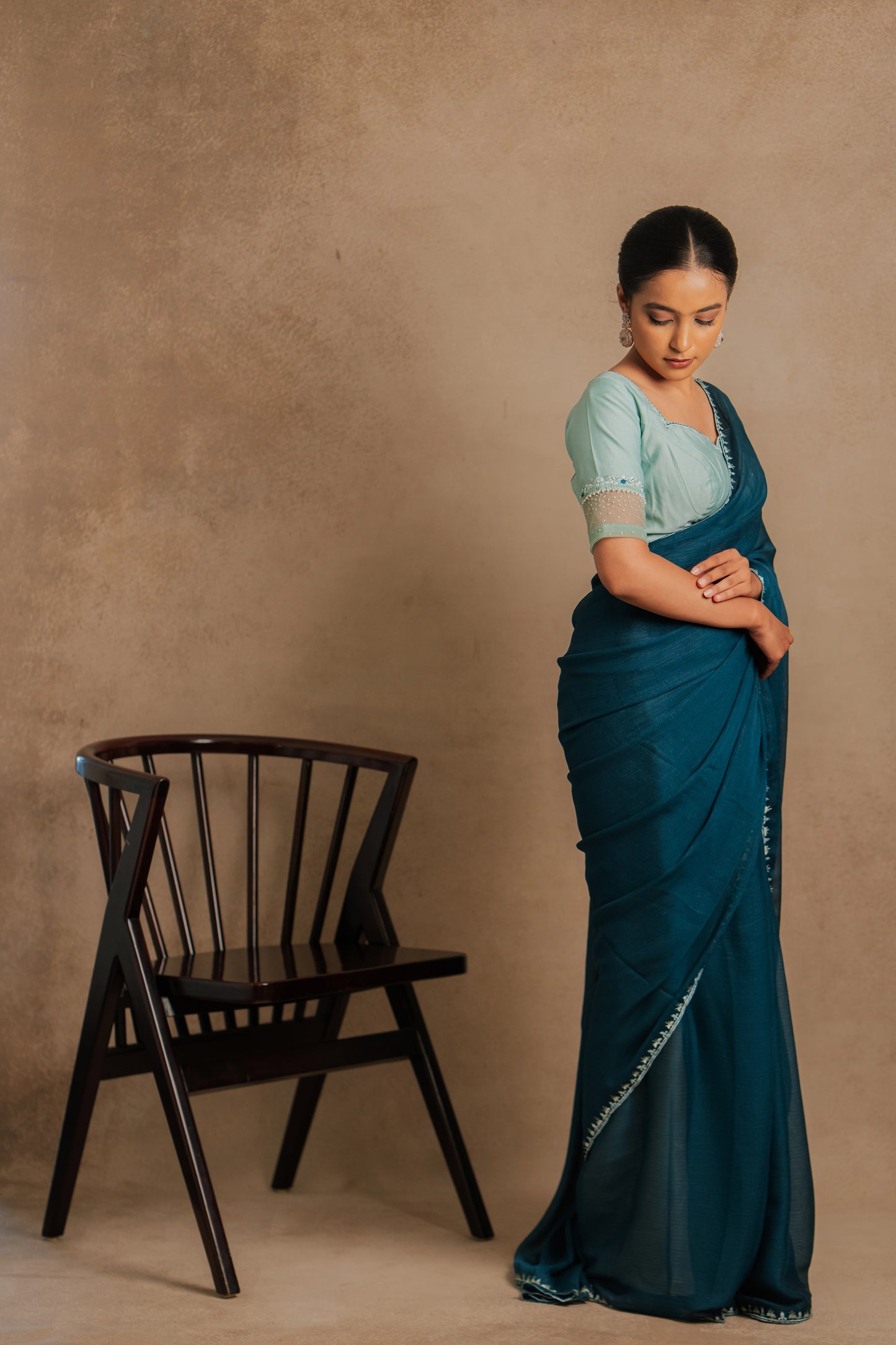 Model Krisha in a photoshoot in embroidered shimmer chiffon saree in teal paired with a chanderi blouse in muted turquoise with pearl beads detailing by team AKloset.