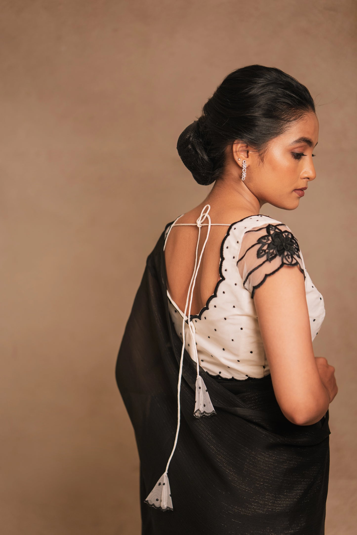 Model Krisha posing for back blouse design in an embroidered shimmer chiffon saree in black paired with a resham embroidered white tulle blouse by team AKloset.